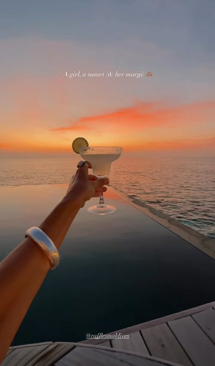 a hand holding a wine glass on the edge of a boat at sunset or sunrise