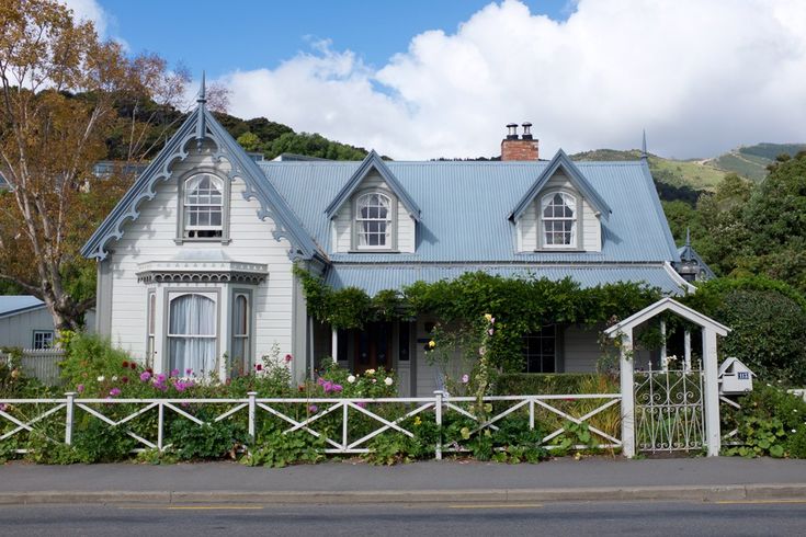 a white house with blue roof surrounded by greenery and flowers on the side of the road