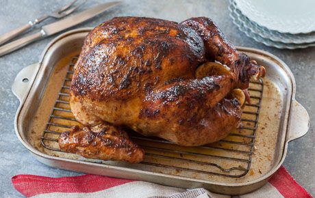 a roasted chicken sitting on top of a metal pan next to a fork and knife