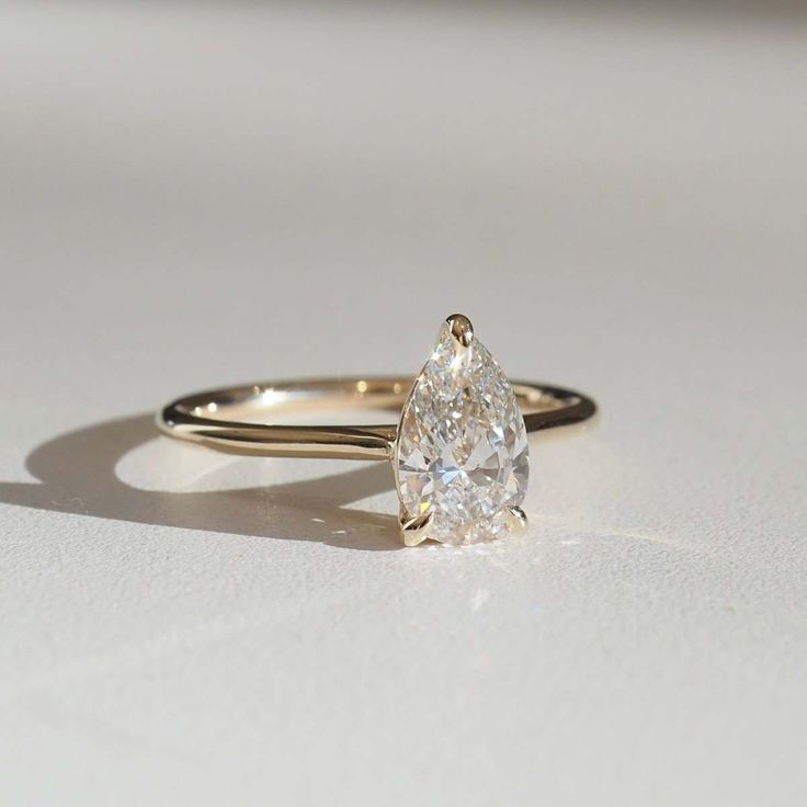 a pear shaped diamond ring sitting on top of a white surface with the light reflecting off it's side