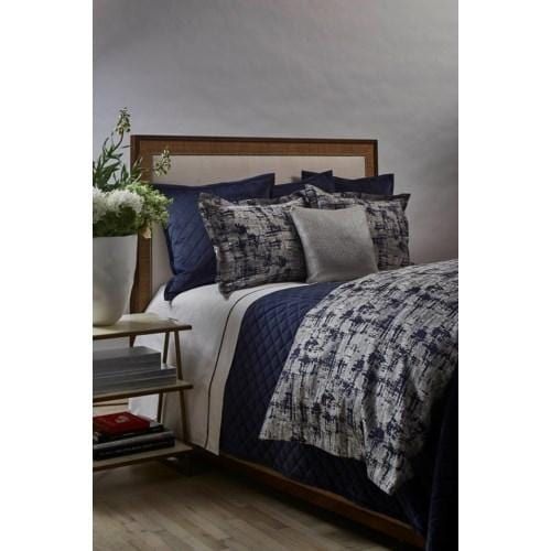 a bed with blue and white comforters in a bedroom next to a nightstand on a wooden floor