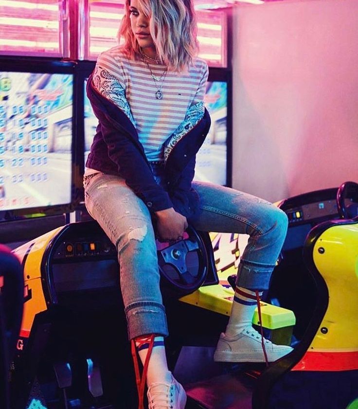 a woman sitting on top of a toy car in front of two televisions with neon lights