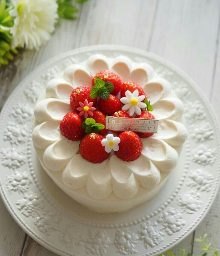 a white cake topped with strawberries on top of a white plate next to flowers