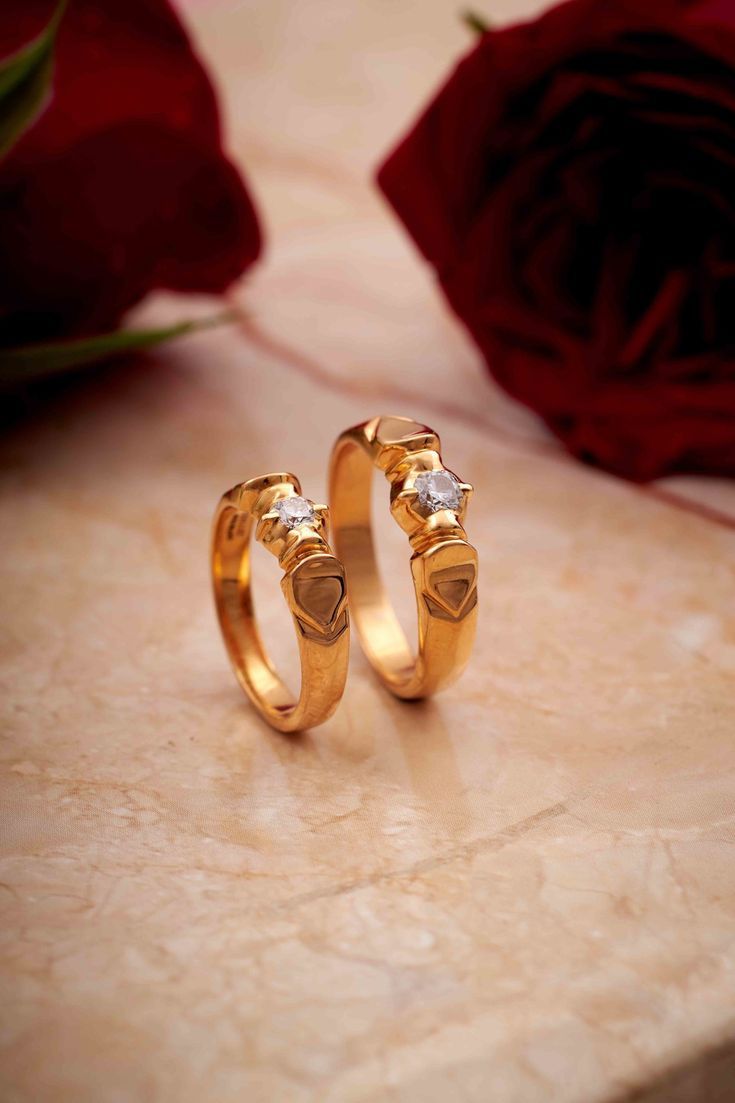 two gold wedding rings sitting on top of a marble table next to a red rose