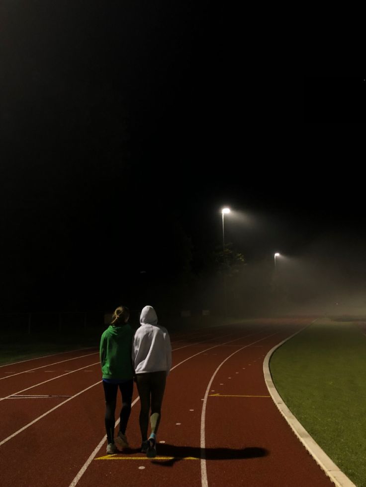 two people standing on a track at night with fog coming off the ground behind them