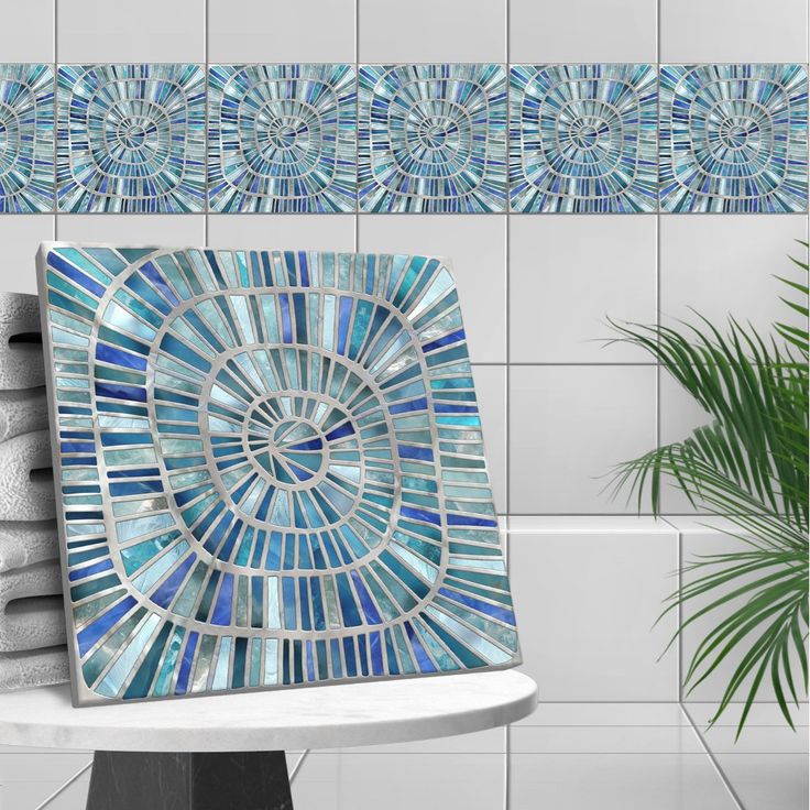 a blue mosaic tile design on a wall next to a potted plant and towel rack