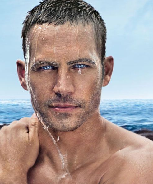 a man with blue eyes and no shirt on is staring at the camera while standing in front of an ocean