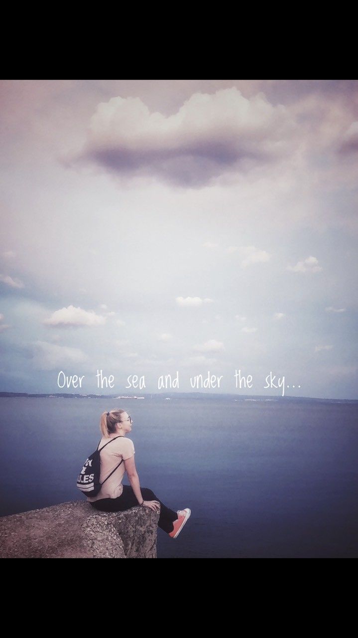 a woman sitting on top of a rock next to the ocean under a cloudy sky