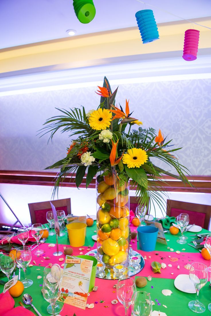 a vase filled with fruit and flowers on top of a table covered in paper decorations