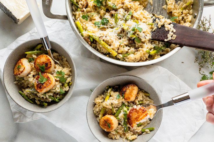 two bowls filled with shrimp and rice on top of a white table next to silver utensils