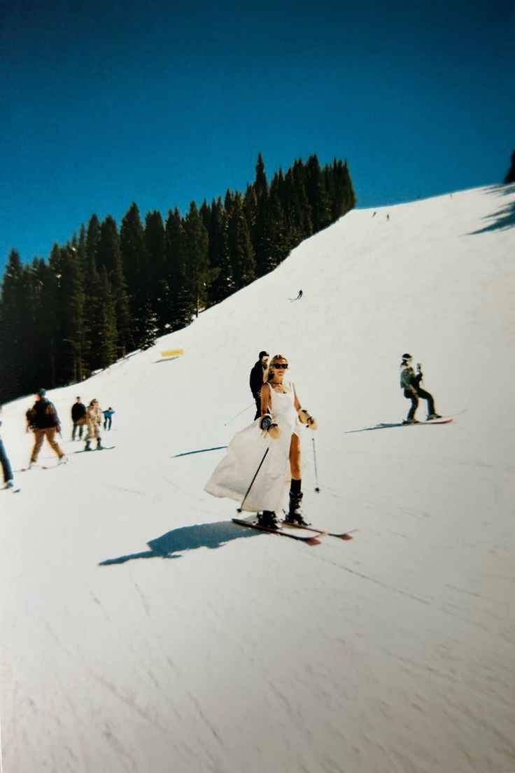 a bride and groom on skis in the snow with other skiers behind them