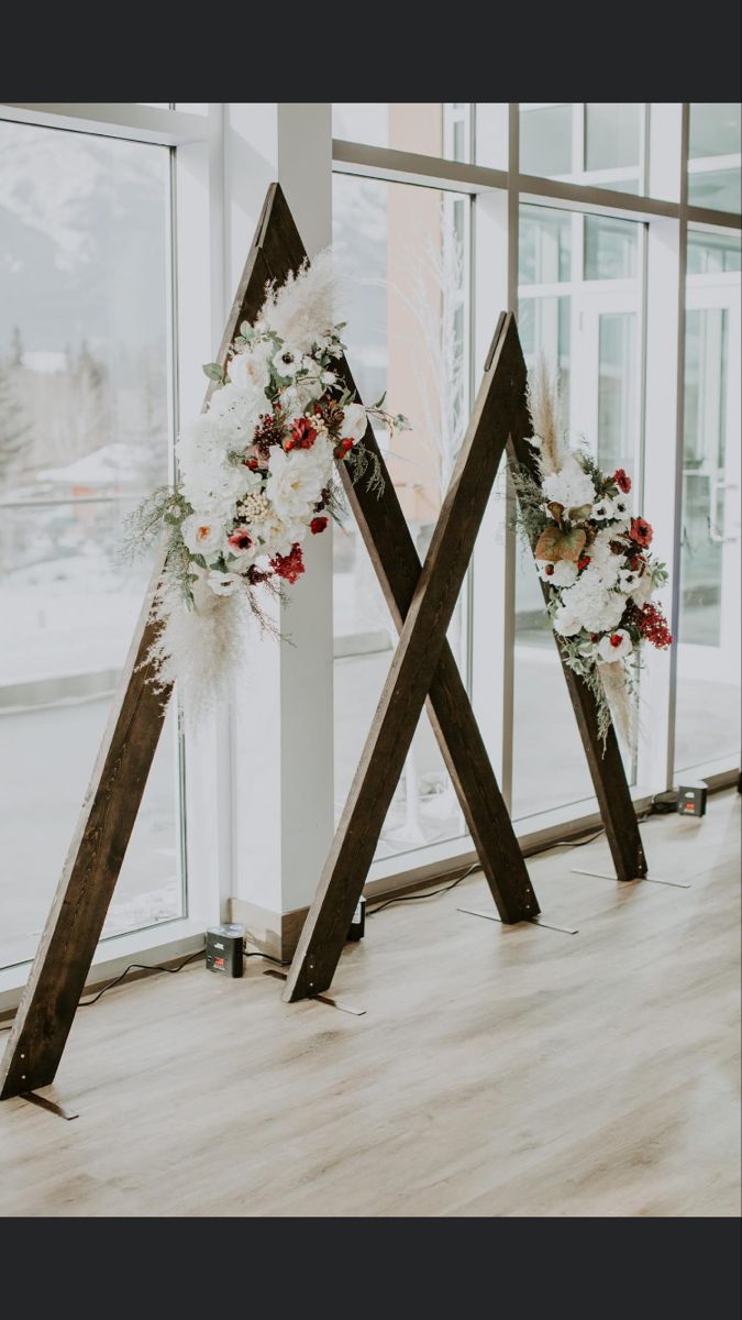 three wooden crosses decorated with flowers in front of large windows and snow covered mountains behind them