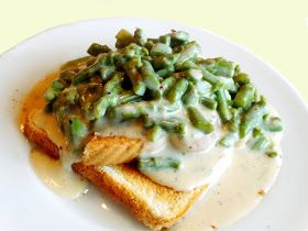 a white plate topped with french fries covered in green beans and gravy on top of bread