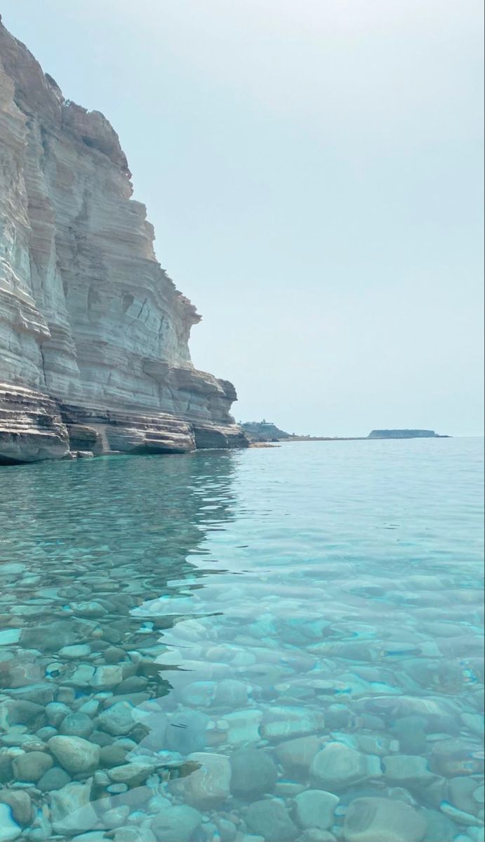 the water is crystal blue and there are rocks on the shore near the cliff face