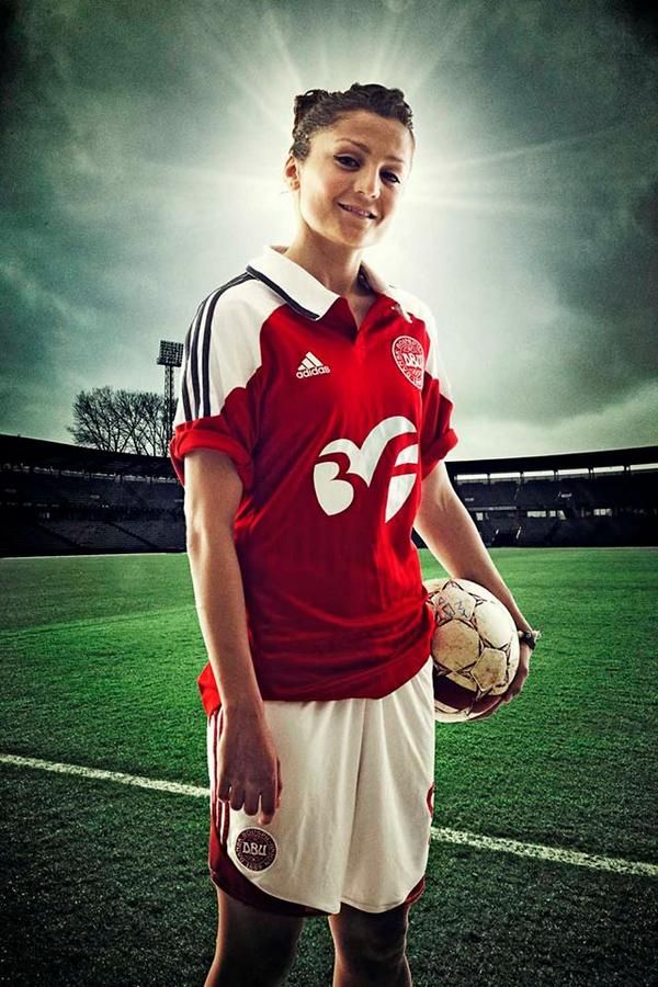 a young woman holding a soccer ball and wearing a red jersey on a green field