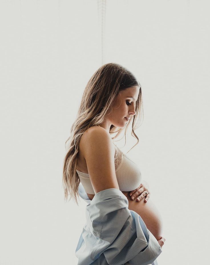 a pregnant woman is standing in front of a window with her hands on her stomach