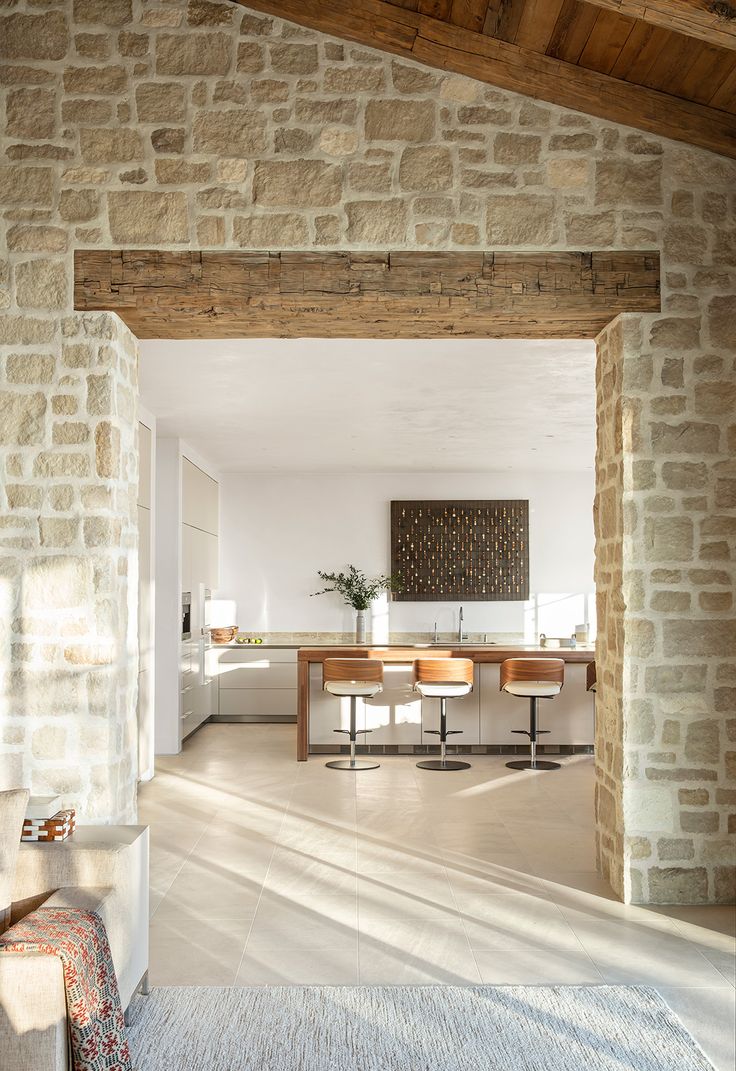 an open door leading to a kitchen and dining room with white walls, wood beams and flooring