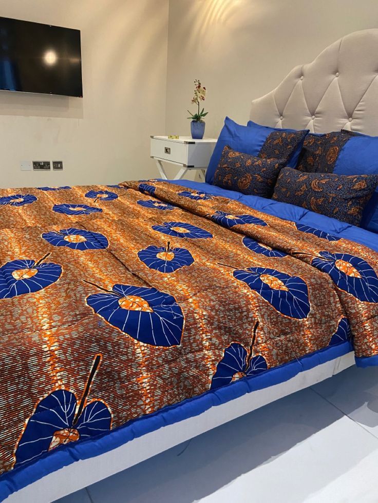 a bed with an orange and blue comforter on top of it next to a flat screen tv