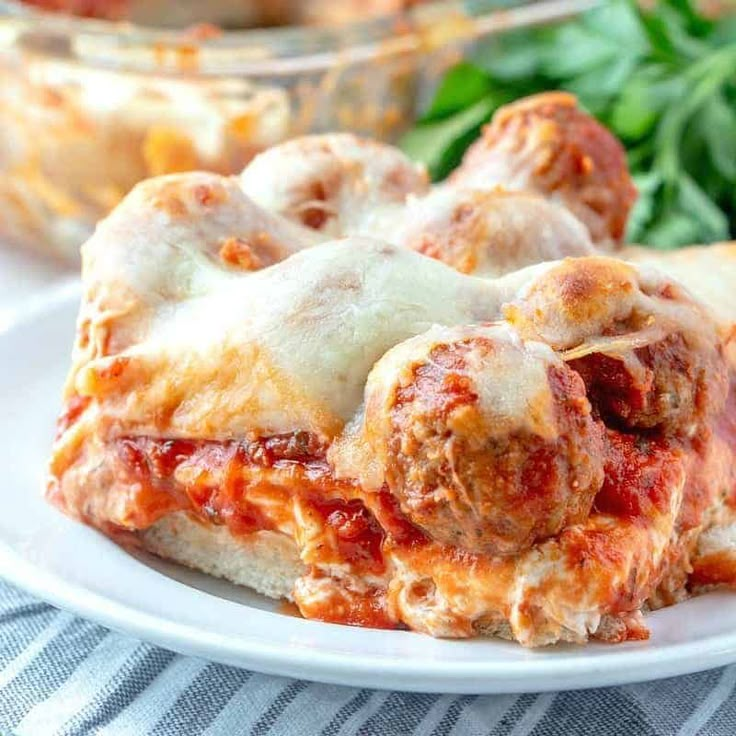 a white plate topped with lasagna covered in sauce and cheese next to a bowl of spinach