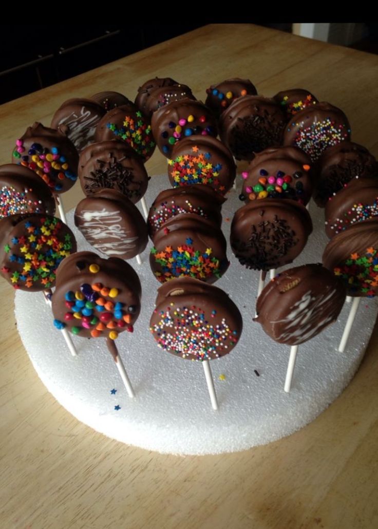 chocolate covered cake pops with sprinkles on a white plate sitting on a wooden table