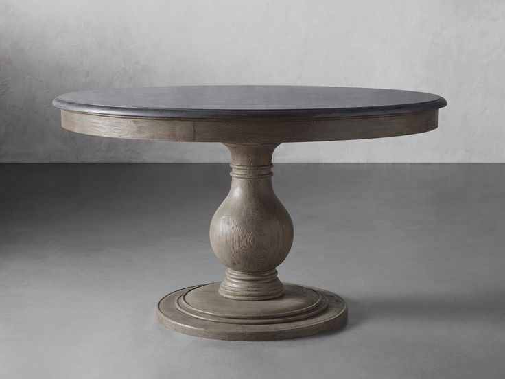 a round wooden table sitting on top of a cement floor next to a white wall