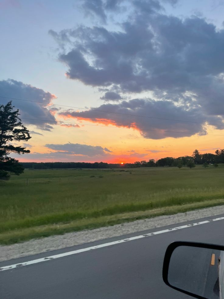 the sun is setting over an open field as seen from inside a car's side view mirror