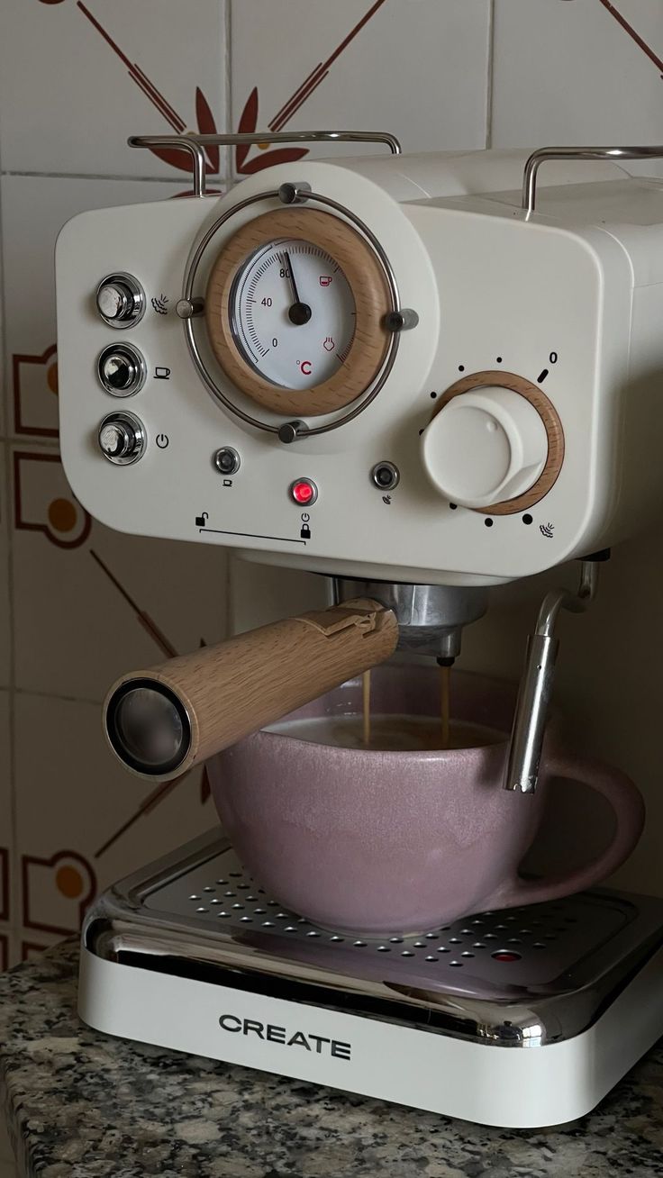 a white coffee machine with a pink bowl and wooden spoon in front of it on top of a counter