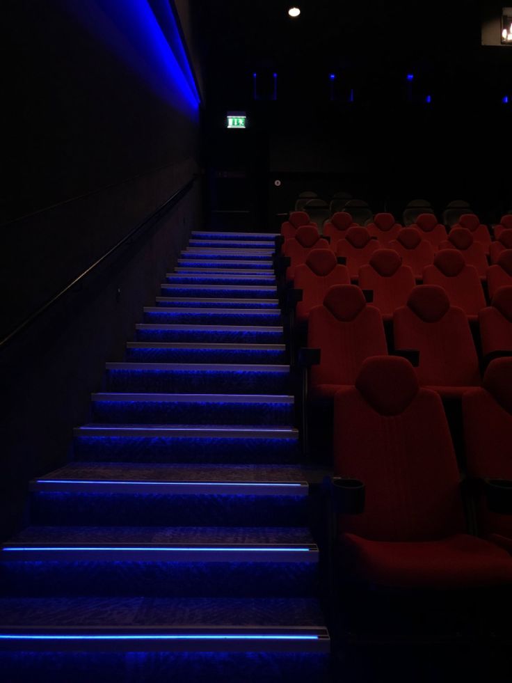 an empty auditorium with red seats and blue steps leading up to the screen on the wall