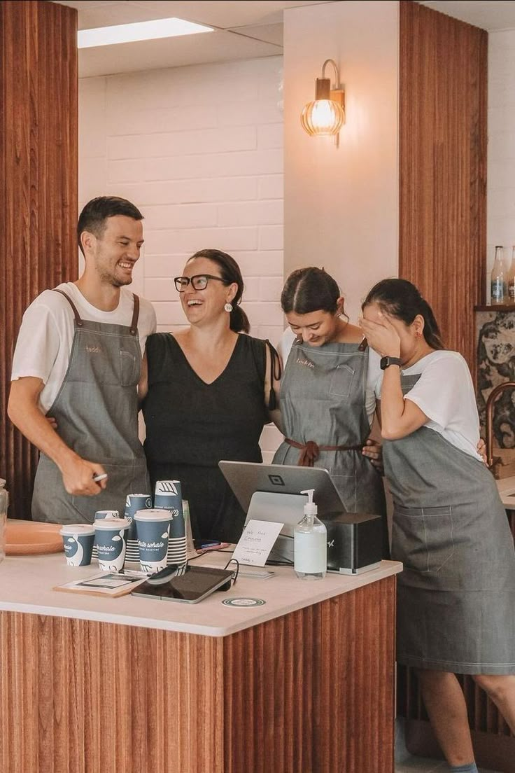 three people standing in front of a counter with cans of sodas on it and one person using a laptop