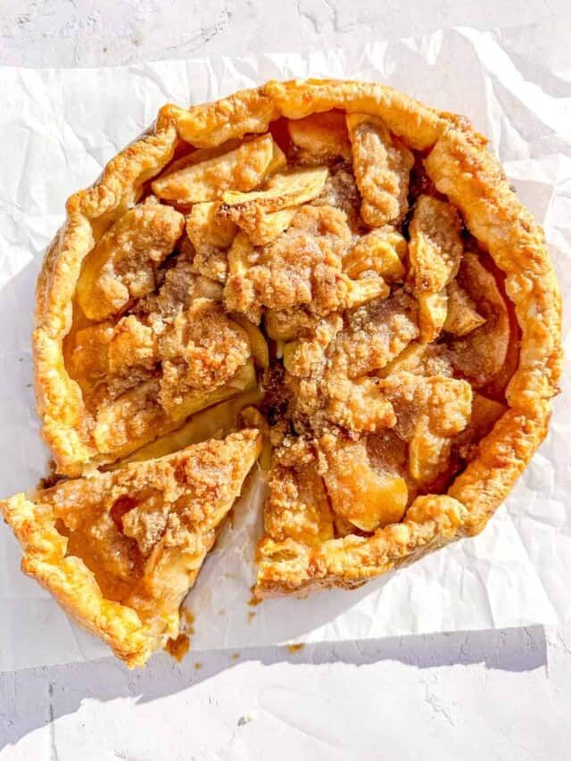 an apple pie is cut into pieces on top of white paper with crumbs