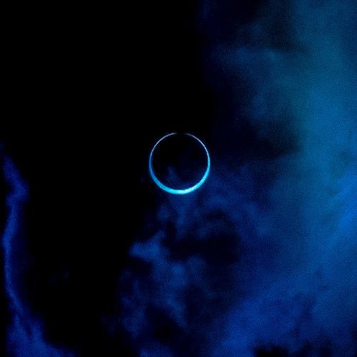 an eclipse in the night sky with clouds and blue light coming from it's center