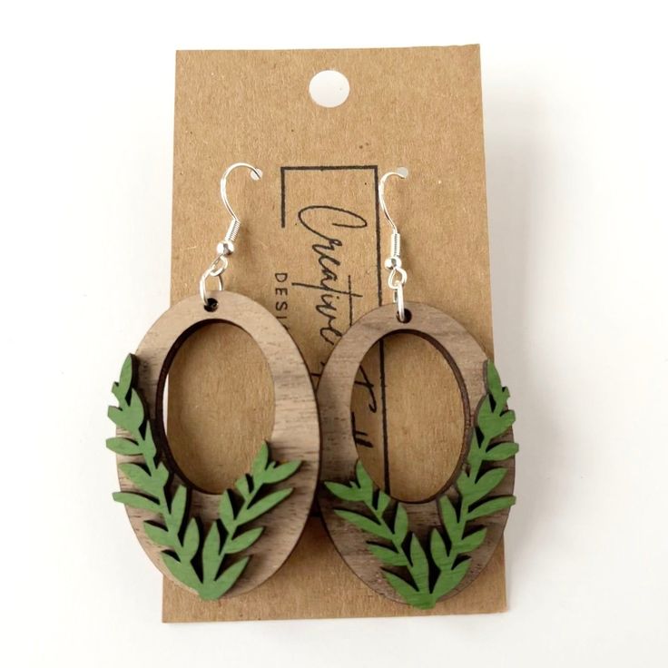 wooden earrings with green leaves on them sitting next to a cardboard package and tagline