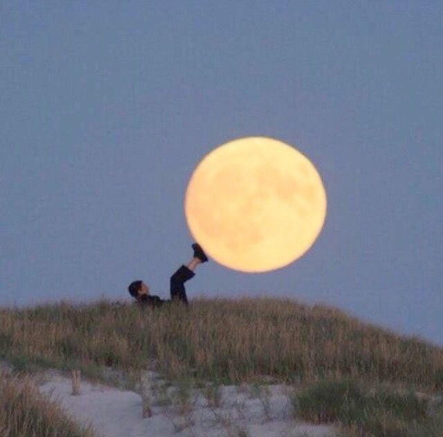 a man laying on top of a grass covered hill under a full moon