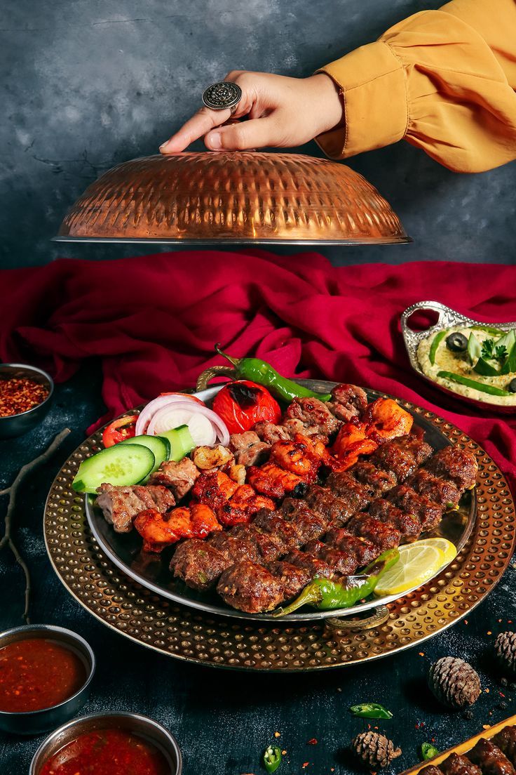 a person holding a platter with meat and vegetables on it next to other dishes