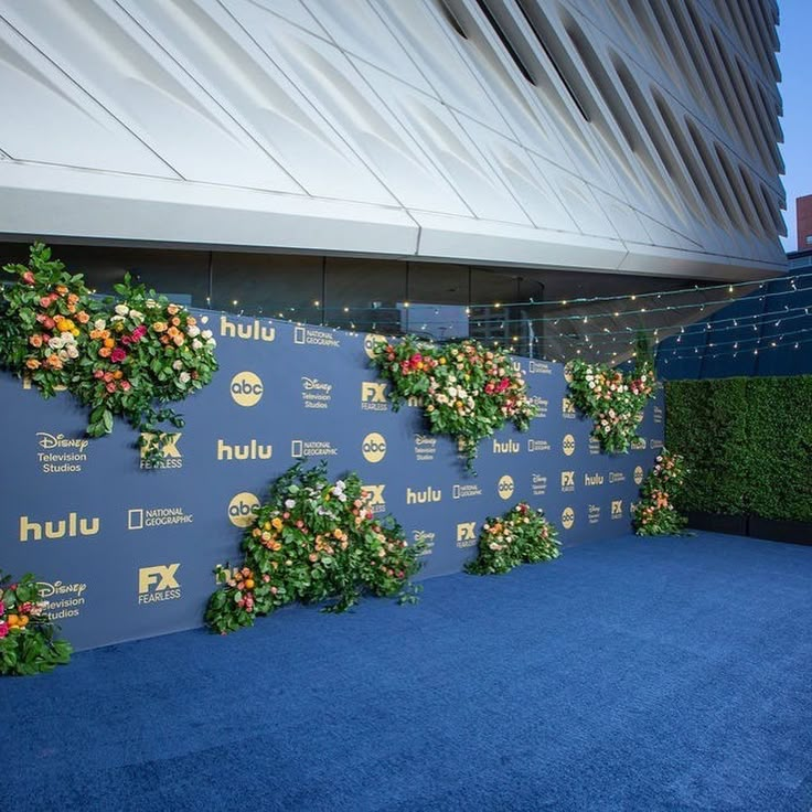 a blue carpeted area with flowers and plants on the wall next to a building