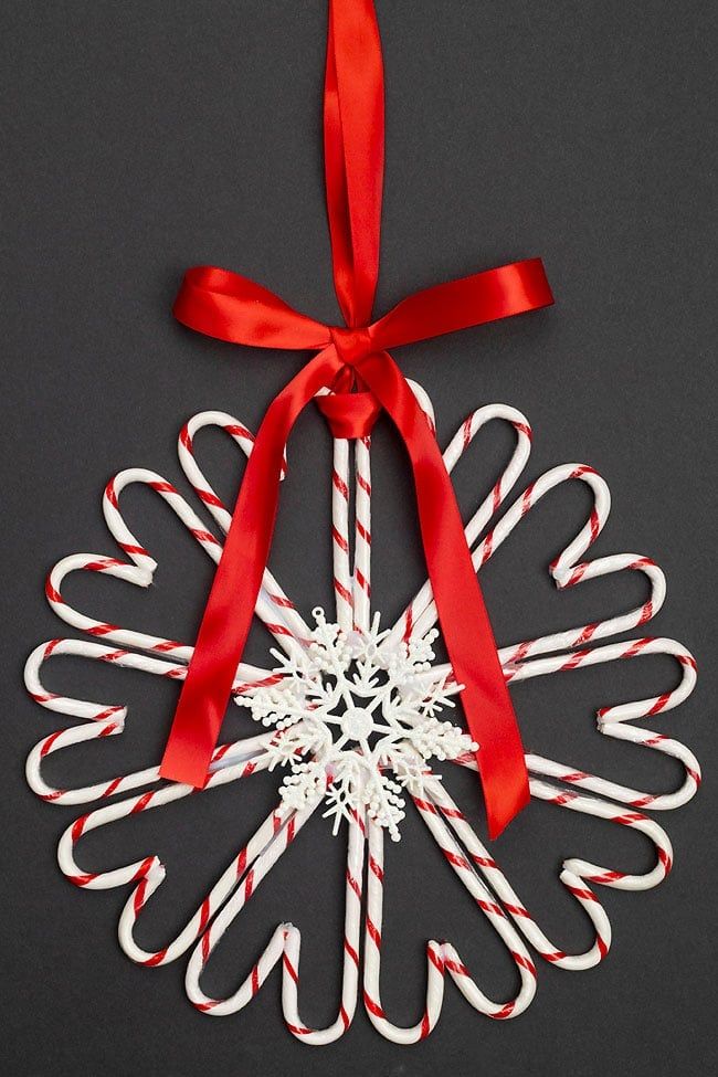 a candy cane snowflake ornament hanging from a red ribbon on a black background