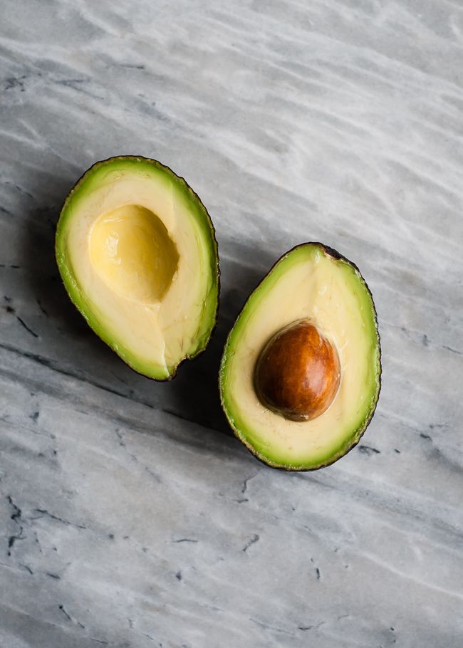 an avocado cut in half on a marble surface