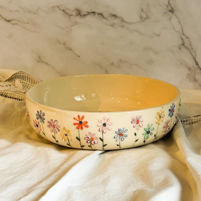 a bowl with flowers painted on it sitting on top of a table next to a lace doily