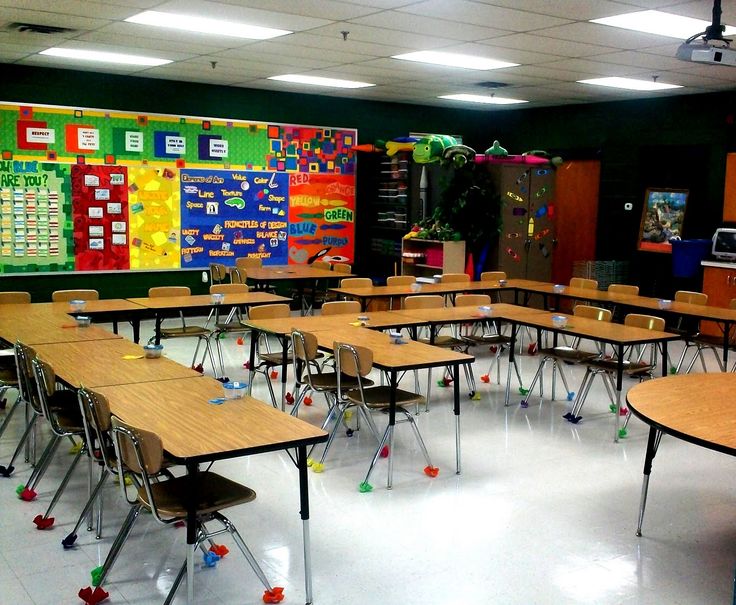 an empty classroom with lots of desks and chairs in front of colorful bulletin boards