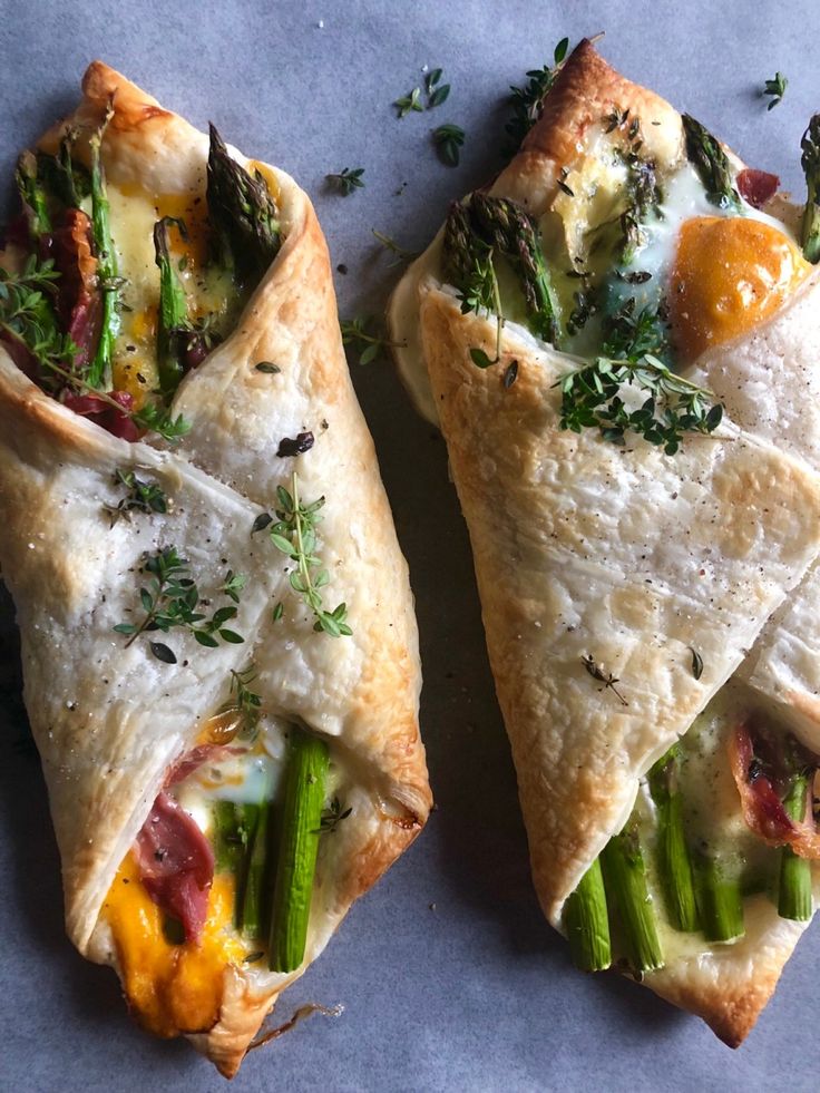 two pieces of pizza with asparagus, bacon and cheese on them sitting on a piece of parchment paper