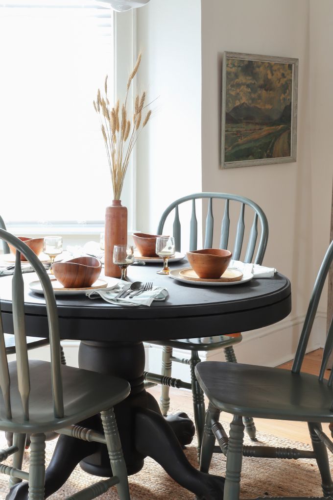 a dining room table with four chairs and plates on top of it in front of a window