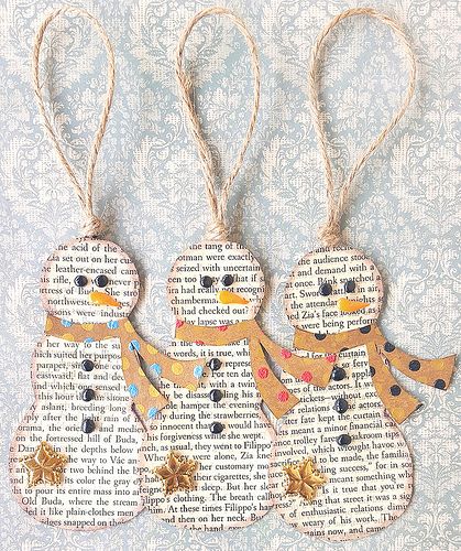 three snowmen made out of old book pages are hanging from twine strings on a wall