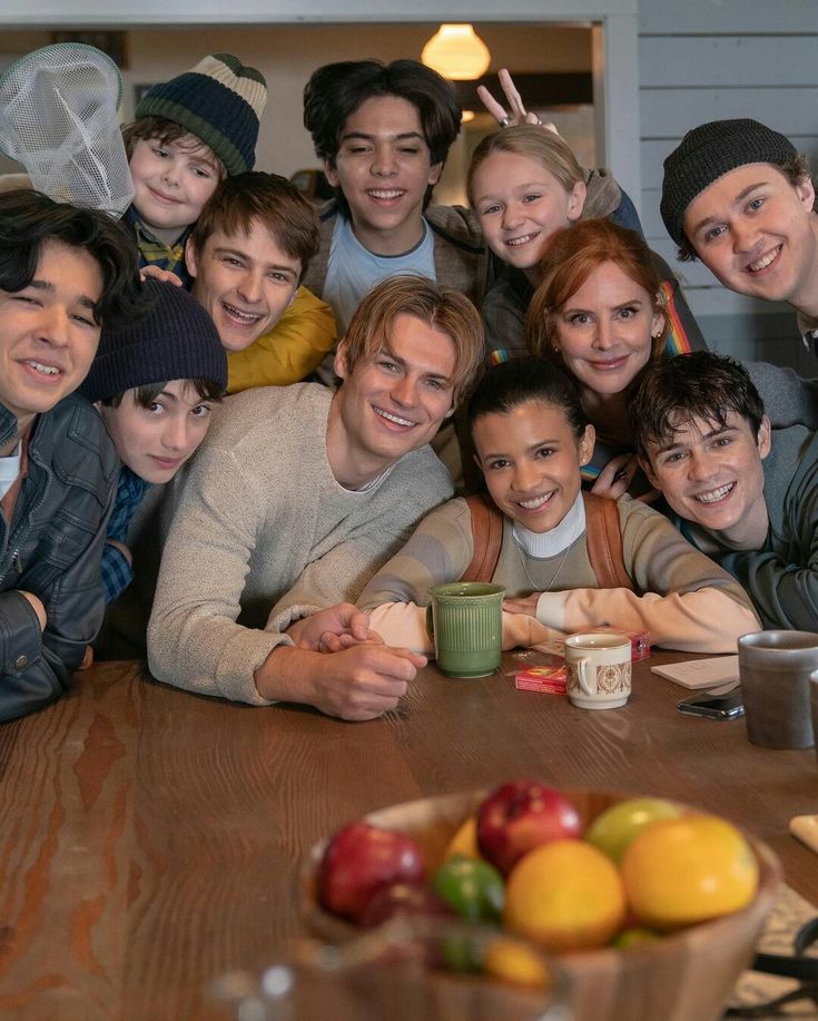 a group of people posing for a photo at a table with apples and oranges