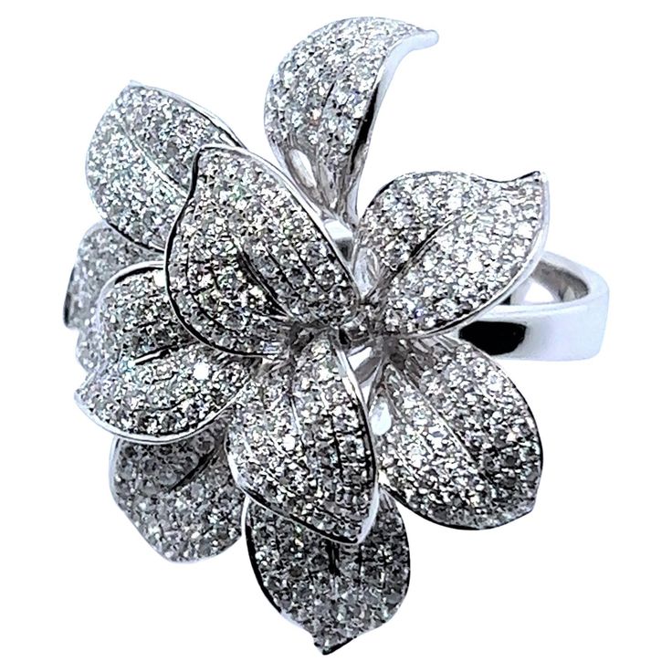 Embodying the essence of style, this diamond flower ring is also a testament to the timeless allure of nature's wonders. Dazzled by the sparkle of 360 brilliant-cut diamonds, it create a captivating play of light and brilliance, reminiscent of the natural sparkle of a blossoming flower. The diamonds are presented in G-H colour and si clarity, with a total weight of 3.65 carats. Seven beautiful petals are crafted in luxurious 18 Karat white gold, a harmonious example of artistic mastery and timeless beauty of a floral world. Embrace a lucky charm in your collection, allow this symbol of good fortune bring beauty and sophisticated harmony in to your life. Assay Mark: D 365 Makers Mark: G 18K Diamonds: 360 BR, H-G, si, tot. 3.65 carats Dimensions: 35 mm x 38 mm / 1.37 in x 1.49 in Weight: 20. Luxury Cubic Zirconia Flower Diamond Ring, Luxury Gemstone Rings In Flower Shape, Luxury Classic Flower Cluster Ring, Luxury Gold Flower Ring With Brilliant Cut, Luxury Dazzling White Gold Flower Ring, Blossoming Flower, Wedding Jewellery Designs, Diamond Flower Ring, Flower Diamond Ring