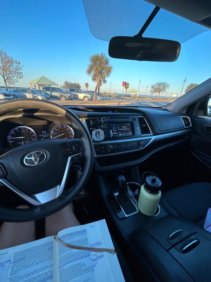 the interior of a car with an open book and cup on the steering wheel, in front of palm trees