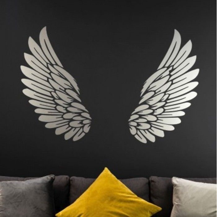 two white wings on a black wall above a gray couch with yellow pillows and throw pillows