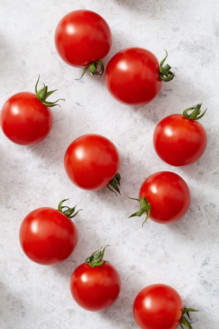 six tomatoes laid out on a white surface