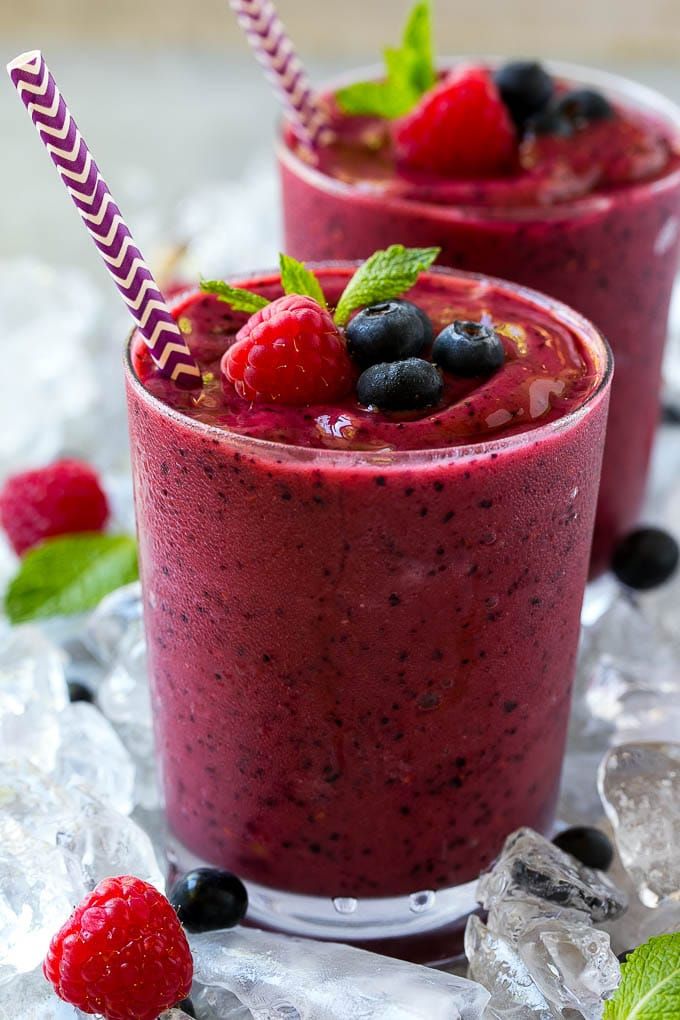 two smoothies with berries and mint garnish are on top of crushed ice