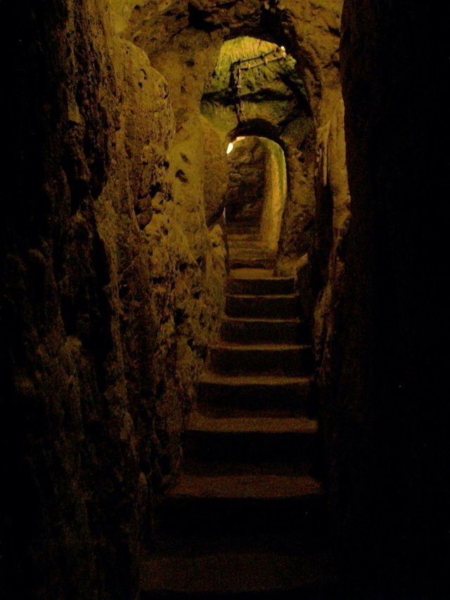 the stairs lead up to an underground passage in a stone wall with light coming from it