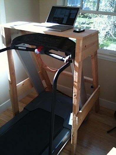 a laptop computer sitting on top of a wooden desk next to a treadmill in front of a window